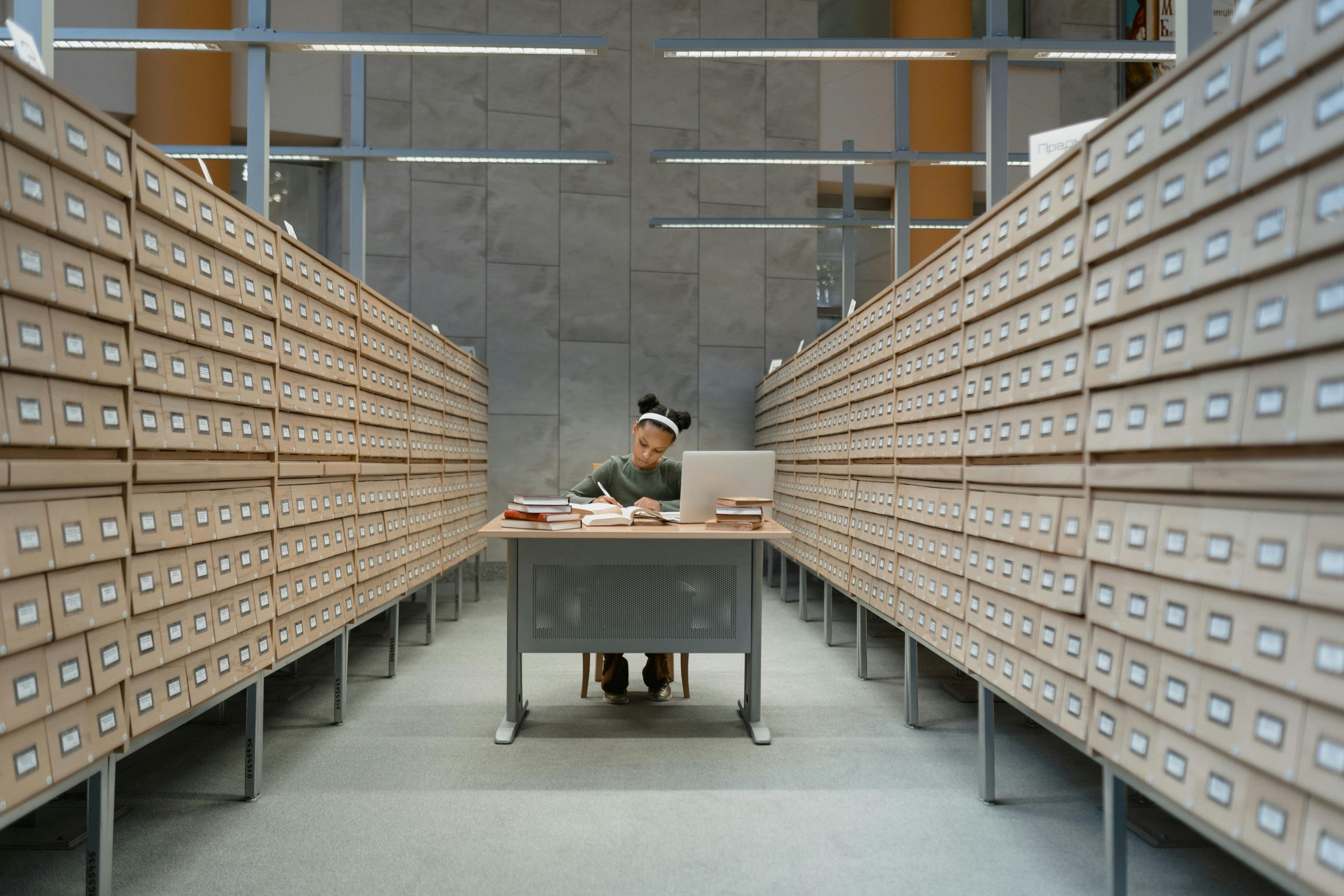 Student diligently studies at a desk surrounded by library card catalogs, focusing on her work.