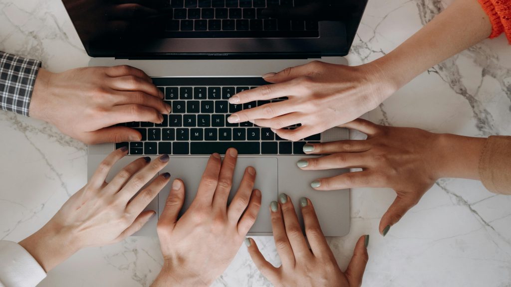 Top view of multiple hands typing on a laptop, showcasing teamwork and diversity.